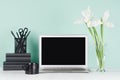 Modern business interior - workplace with blank computer display, black stationery, books, coffee cup, white spring bouquet.