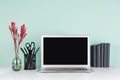 Modern business interior - workplace with blank computer display, black stationery, books, red branch in light green mint menthe.