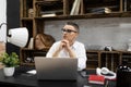 modern business woman in glasses with a short haircut sits at her desk in front of a laptop thinking Royalty Free Stock Photo