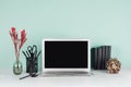 Modern business workplace with blank computer display, black stationery, books, sheaf of dry brown branches, red branch in green.