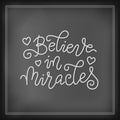 Modern calligraphy lettering of Believe in miracles in white with hearts on chalk background