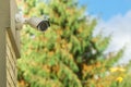 Modern CCTV security camera on building wall, foliage background