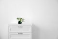 Modern chest of drawers with fresh flowers near wall