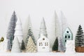 Modern christmas scene, miniature snowy village on white table. Merry Christmas! Stylish little Christmas trees and house