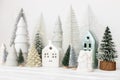 Modern christmas scene, miniature snowy village on white table. Merry Christmas! Stylish little Christmas trees and house