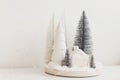 Modern christmas scene, miniature snowy village on white table. Merry Christmas! Stylish little Christmas trees and house. Winter