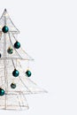 Modern Christmas tree made of silver metal wire, wrapped in a glowing garland and decorated with green balls