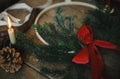 Modern christmas wreath with fir branches and red bow on rustic wooden table with candle, ribbons, pine cones. Atmospheric moody Royalty Free Stock Photo