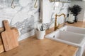 Modern classic kitchen interior with kitchen appliances and white ceramic sink with gold mirror faucet on wood top with marble wal Royalty Free Stock Photo