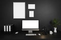 Modern clean office workspace with computer screen and empty isolated frames on dark concrete wall; 3D Illustration