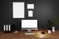 Modern clean office workspace with computer screen and empty isolated frames on dark concrete wall; 3D Illustration