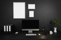 Modern clean office workspace with computer screen and empty isolated frames on dark concrete wall; 3D Illustration
