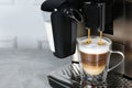 Modern coffee machine making latte into glass cup on grey table, closeup. Space for text Royalty Free Stock Photo