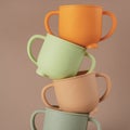 Modern colorful pastel silicone cups stacked in column on brown background. Baby tableware, first feeding.