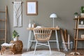 Modern composition at boho interior of home office room with wooden desk, stylish armchair, bamboo shelf, carpet, macrame. Royalty Free Stock Photo