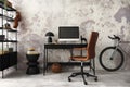 Modern composition of concrete office interior with black desk, stylish brown armchair, computer screen, bike, black simple lamp, Royalty Free Stock Photo