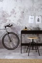 Modern composition of indiustral concrete office interior with black desk, stylish stool, bike, books, gray concrete wall, boho Royalty Free Stock Photo