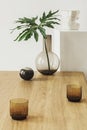 Modern composition of living room interior with wooden table, tropical leaf in vase, candelstick, decoration.