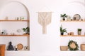 Modern composition of wabi sabi interior with shelf with home decoration and macrame.