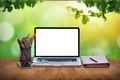 Modern computer laptop with blank screen, notepad and office stationery on table with bokeh green garden background Royalty Free Stock Photo