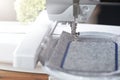 modern computerised sewing machine with embroidery unit stitching a blue frame on grey felt in a friendly work environment Royalty Free Stock Photo