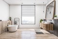 Modern concrete and wooden luxury bathroom interior with bright window and city view, various objects. Hotel and luxury home