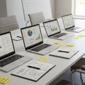 A modern conference room features a long table with four open laptops displaying