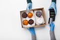 Modern contactless payment for order. Courier in rubber gloves gives terminal and box of muffins and coffee, client Royalty Free Stock Photo