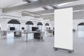 Modern coworking office interior with empty white mock up roll up poster, computer screens on desks, concrete flooring and window Royalty Free Stock Photo