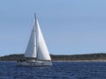 A modern cruise sailing yacht with a Bermuda sloop-type rig goes past the green coast of the Croatian Riviera on a sunny summer da