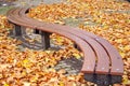 Modern curve bench with autumn leaves on the pavement