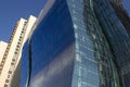 Modern curved blue corporate building next to a yellowish classical one.