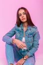 Modern cute fashion model young woman in denim jacket in vintage jeans in stylish t-shirt relaxes and smiling near pink wall Royalty Free Stock Photo