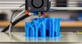 Modern 3D printer actively printing a blue cylindrical object in a workshop environment Royalty Free Stock Photo