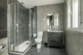 Modern design toilet with gray tiles and floors, gray wooden furniture and a shower cabin with glass partitions