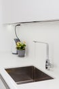 Modern designer chrome water tap over stainless steel kitchen sink. Interior of bright white kitchen. Royalty Free Stock Photo