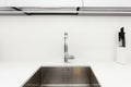 Modern designer chrome water tap over stainless steel kitchen sink. Interior of bright white kitchen. Royalty Free Stock Photo