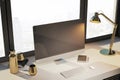 Modern designer desktop with empty computer monitor, lamp, supplies and other items. Window with city view in the background. Mock Royalty Free Stock Photo