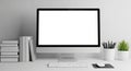 Modern desktop computer setup with a blank white screen on a white desk with books and plants Royalty Free Stock Photo