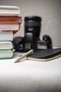 Modern digital SLR camera on the table next to a stack of books, and in the foreground a notebook and pencil. Royalty Free Stock Photo