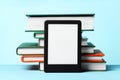 Modern e-book reader and stack of hard cover books on light blue background