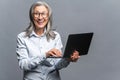 Modern elderly senior woman in formal wear using laptop computer isolated on gray. Portrait of mature female office Royalty Free Stock Photo