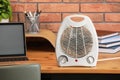 Modern electric fan heater near laptop and notebooks on wooden table in office Royalty Free Stock Photo