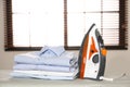 Modern electric iron and folded clothes on board