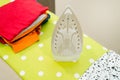 Modern electric iron and pile of clothes on ironing board Royalty Free Stock Photo