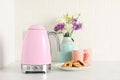 Electric kettle, bouquet, cookies and cups on counter in kitchen