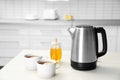 Modern electric kettle, cups of tea and honey on table in kitchen