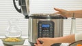 Modern electric multi cooker close up on kitchen table. Woman pushing button