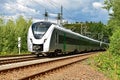 A modern electric regional train runs on a multi-lane track through natural surroundings