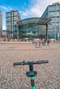 Modern electric scooter in front of modern steel and glass buildings and main train station Haupt Bohnhoff and traveling people